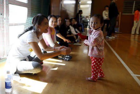 A 1-year-old Cambodian girl (R) and Cambodian residents in Japan cheer on their volleyball team during Asia Sports Festa in Yokohama, south of Tokyo, Japan, October 25, 2015. REUTERS/Yuya Shino/Files