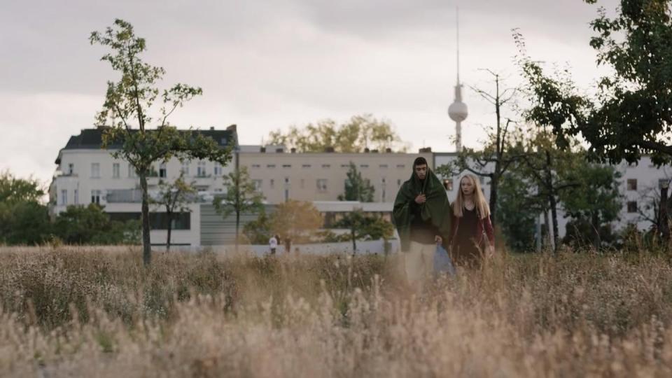 Dos jóvenes atraviesan un campo con Berlín al fondo.