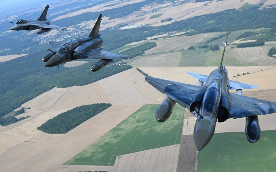 Three Mirage jets, seen in flight from above, with fields far below them