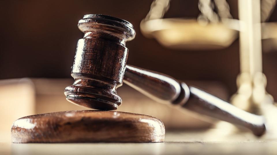 A wooden judges' gavel in the foreground with a golden set of scales in the backgroundr