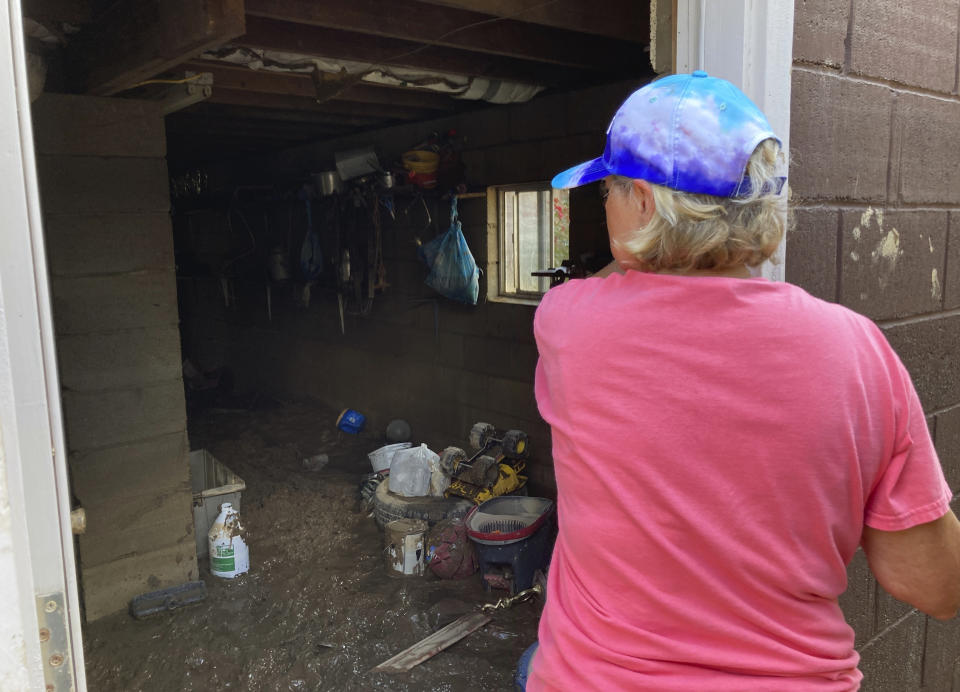 Brenda Francis peers into the muddy basement of her home in Garrett, Ky., Saturday, July 30, 2022. Francis is tired of the area's flooding and wants to move away, to be closer to her grandchildren. The tiny town of Garrett was completely under water when floodwaters struck eastern Kentucky last week. (AP Photo/Dylan Lovan)