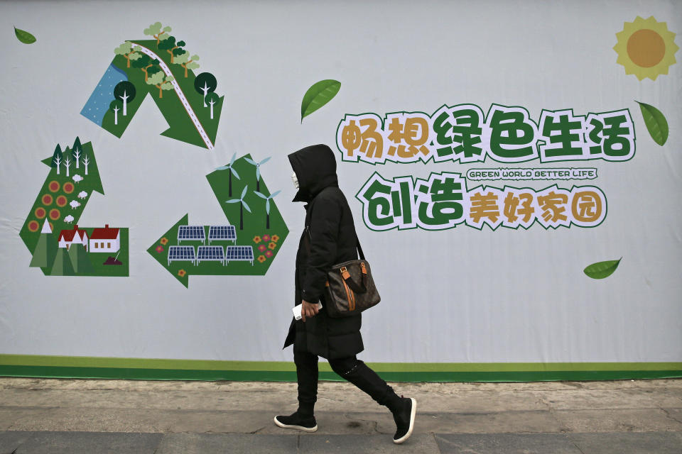 A woman wearing a mask against pollution walks by a poster promoting environment protection on display at a sidewalk in Beijing, Wednesday, Dec. 5, 2018. The climate change conference, COP24, takes place in Katowice, Poland, from Dec. 2-14, 2018. (AP Photo/Andy Wong)