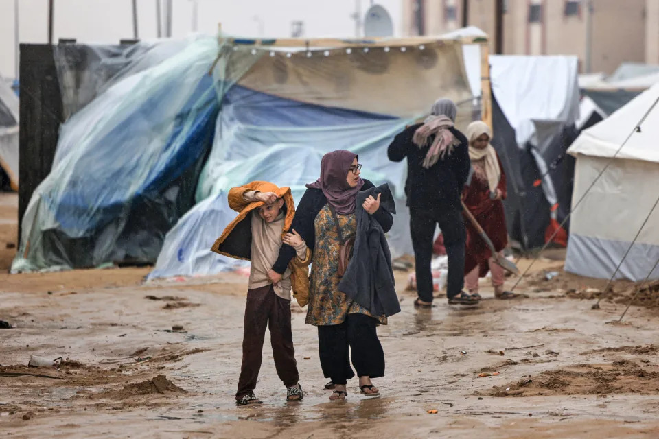 Palestinians walk under the rain at a camp for displaced people in Rafah, in the southern Gaza Strip where most civilians have taken refuge, on Dec. 13, 2023. (Mahmud Hams / AFP via Getty Images)