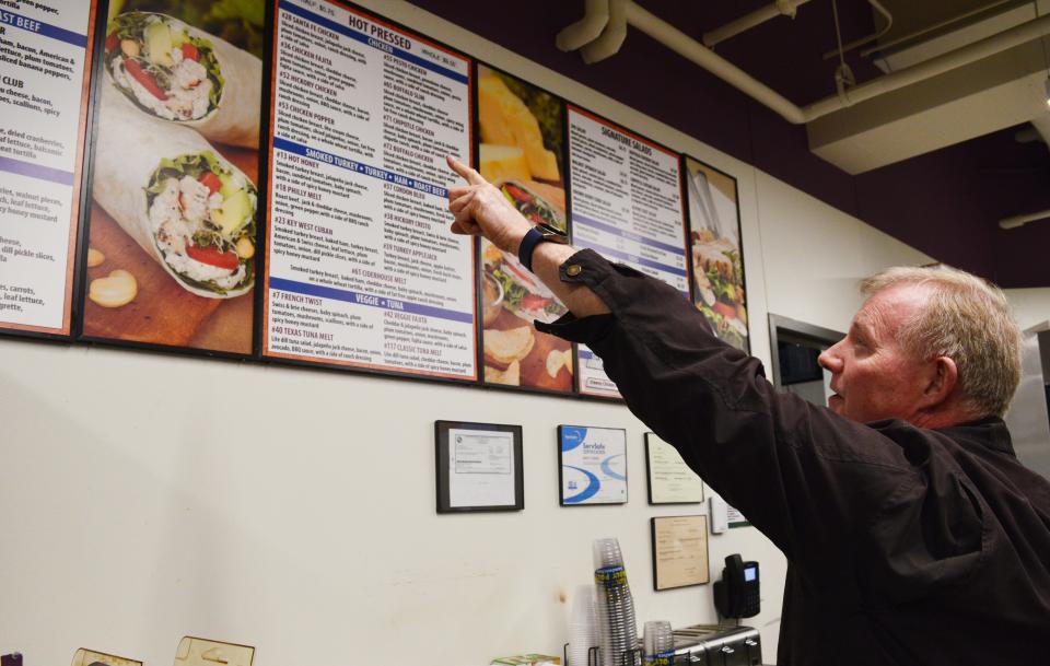 Tom Seybert, owner of the Roly Poly Sandwich shop at Ivy Tech Bloomington, points to one of the favorite sandwiches on Feb. 22, 2024.