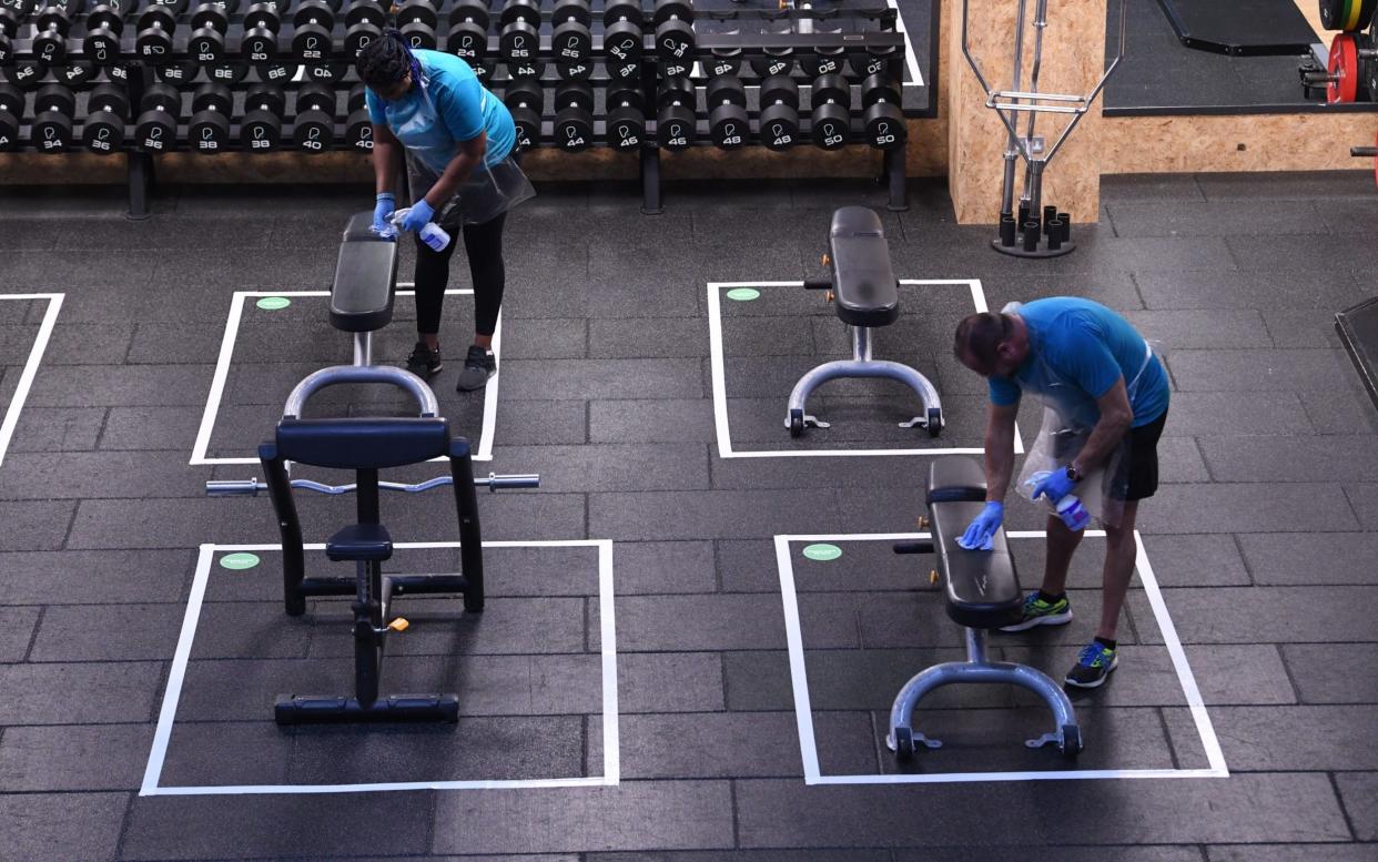 Personal trainers clean down socially-distanced exercise equipment in preparation for the reopening of Pure Gym's facility at Park Royal, west London - Russell Sach