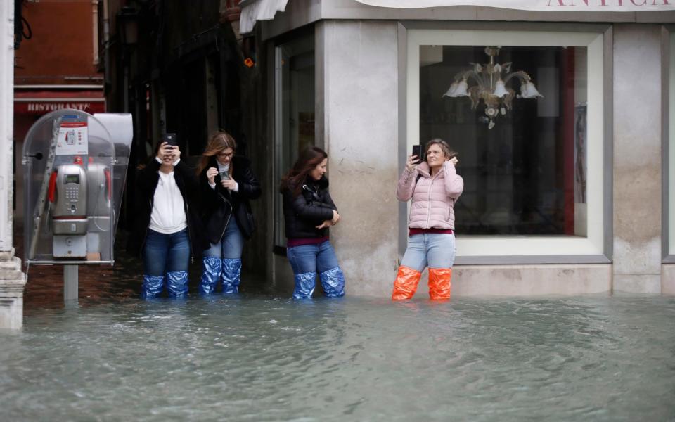 Tourists in plastic waders take photos of the flooding in Venice  - Luca Bruno/AP