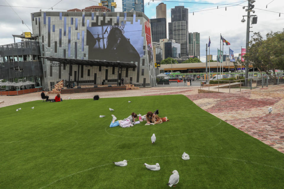 Two women are seen laying down inside a marked circle setup to encourage social distancing at Federation Square in Melbourne, Australia. 