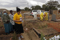 A family watches pallbearers carry the coffin of a relative who died from COVID-19 at a cemetery in Harare, Zimbabwe on Thursday, July 15, 2021. Only about 9% of the population in Zimbabwe has received one dose of coronavirus vaccine amid a surge of the easier-to-spread delta variant. (AP Photo/Tsvangirayi Mukwazhi)