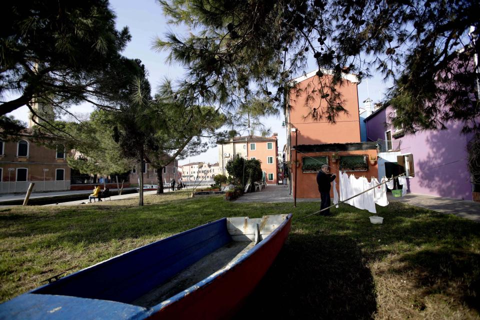 In this image taken on Thursday, Jan. 16, 2020, an elderly man hangs laundry outside his house, at the Burano island, Italy. The Venetian island of Burano's legacy as a fishing village remains the source of its charms: the small colorful fishermen's cottages, traditional butter cookies that were the fishermen's sustenance at sea and delicate lace still stitched by women in their homes. As the island's population dwindles, echoing that of Venice itself, so too are the numbers of skilled artisans and tradespeople who have kept the traditions and economy alive. (AP Photo/Luca Bruno)