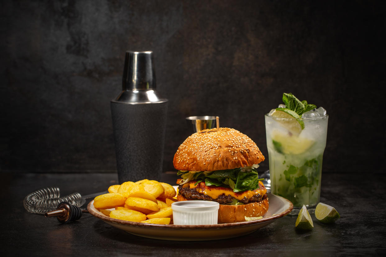 Dinner with burger and glass of mojito cocktail on dark background