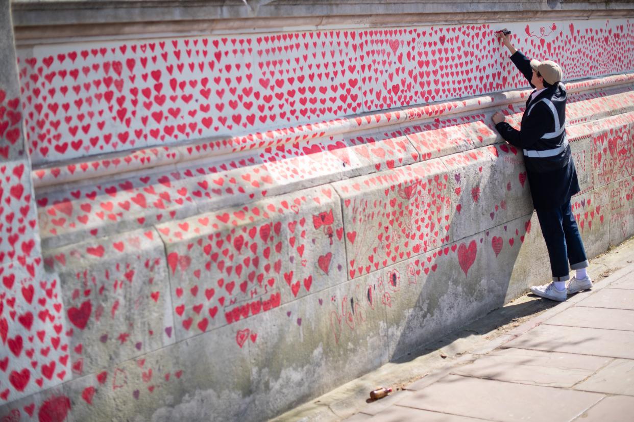 <p>A volunteer adds hearts to the Covid memorial wall in Westminster</p> (PA)