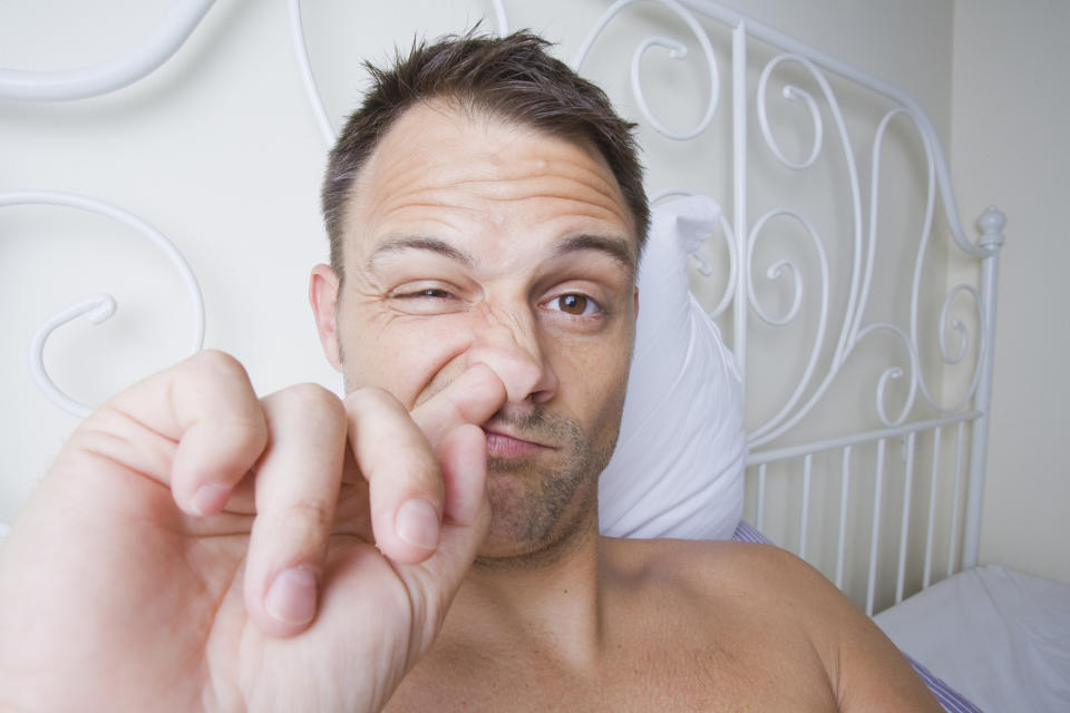 Person in bed making a gesture with their hand simulating small size, winking, with playful expression