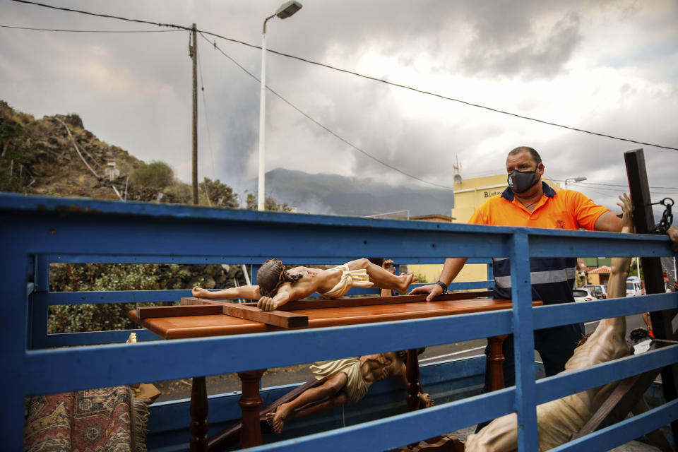 Crucifixes of Jesus Christ lie in the back of a truck after being saved from the San Pio X church in El Paso on the island of La Palma in the Canaries, Spain, Monday, Sept. 20, 2021. Giant rivers of lava are tumbling slowly but relentlessly toward the sea after a volcano, seen in backround, erupted on a Spanish island off northwest Africa. The lava is destroying everything in its path but prompt evacuations helped avoid casualties after Sunday's eruption.(Kike Rincon, Europa Press via AP)