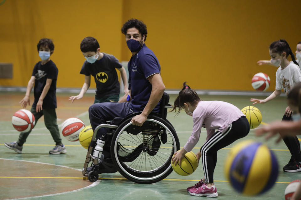 Adolfo Damian Berdun, of Argentina, a professional player and captain of the Argentine basketball Paralympic team, teaches children basketball at a primary school in Verano Brianza, on the outskirts of Milan, Italy, Tuesday, May 11, 2021. Four second-grade classes in the Milan suburb of Verano Brianza have been learning to play basketball this spring from a real pro. They also getting a lesson in diversity. Their basketball coach for the last month has been Adolfo Damian Berdun, an Argentinian-Italian wheelchair basketball champion. Berdun, 39, lost his left leg in a traffic accident at ag 13 in his native Buenos Aires, and he has visited many schools over the years to discuss how he has lived with his disability. (AP Photo/Luca Bruno)