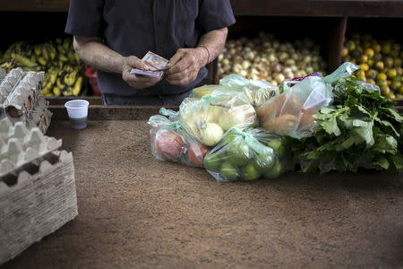 A clerk counts Venezuelan bolivar banknotes after selling goods to a customer at a fruit and vegetable store in Caracas, July 10, 2015. REUTERS/Marco Bello