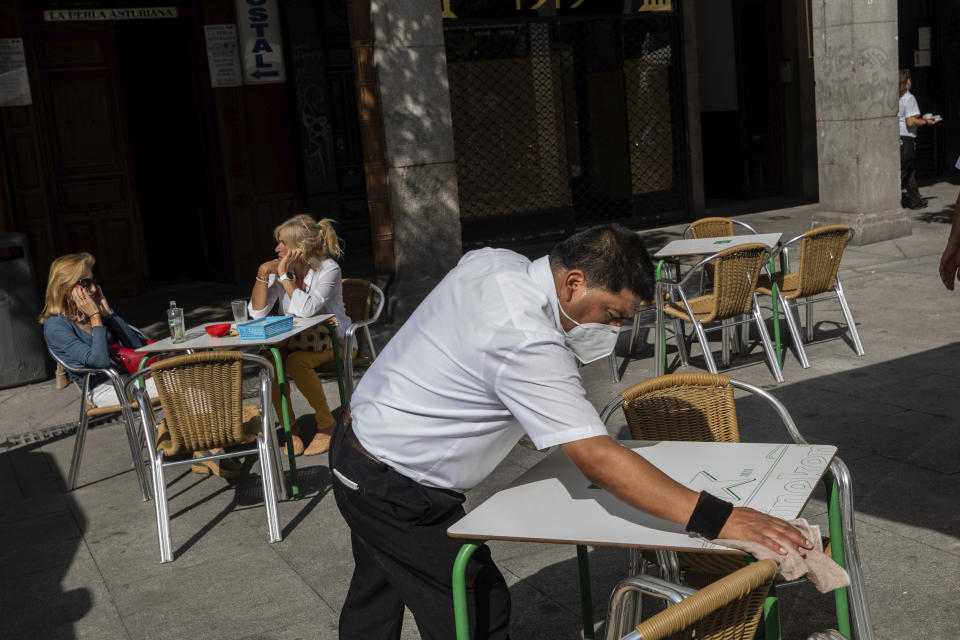 A waiter disinfects a table in downtown Madrid, Spain, Wednesday, Sept. 30, 2020. The Spanish capital and its suburbs, the region in Europe where a second coronavirus wave is expanding by far the fastest, are edging closer to stricter mobility curbs and limits on social gatherings after days of a political row that has angered many Spaniards. (AP Photo/Bernat Armangue)