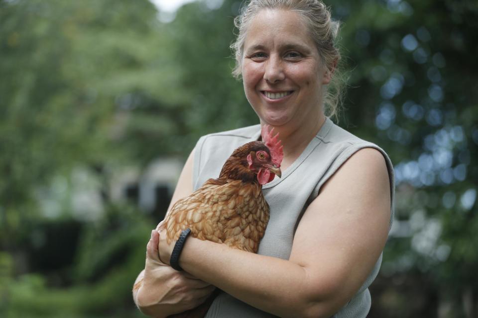 In this Sunday, Aug. 11, 2013 photo, Sandy Schmidt, who owns a portable chicken coop, poses with her chicken, Starlight, at her home in Silver Spring, Md. "Eat local" is the foodie mantra, and nothing is more local than an egg from your own backyard. More and more urban and suburban dwellers are deciding to put up a coop and try chicken farming. (AP Photo/Charles Dharapak)