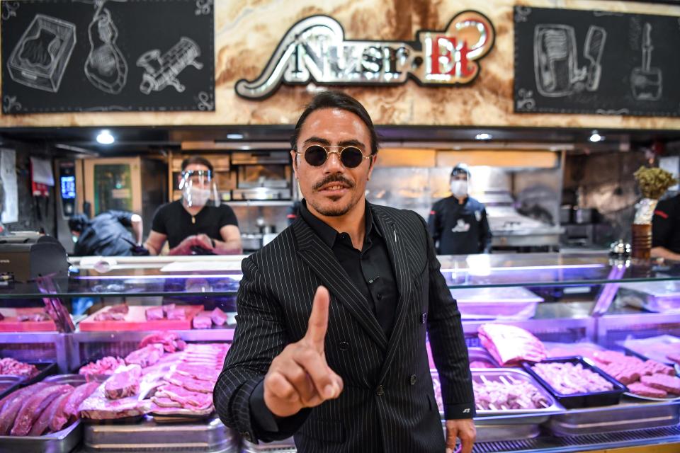 salt bae in front of a case of meat, holding up his pointer finger