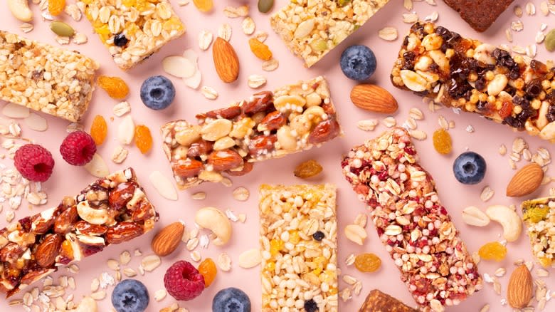 Various granola bars with fresh fruit, nuts, and oats on a pink surface