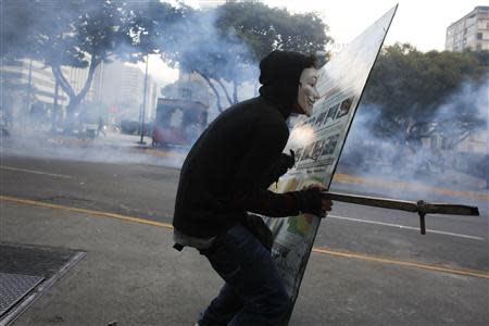 An anti-government demonstrator wearing a Guy Fawkes mask runs with a makeshift shield during clashes with police at Altamira square in Caracas February 27, 2014.REUTERS/Tomas Bravo