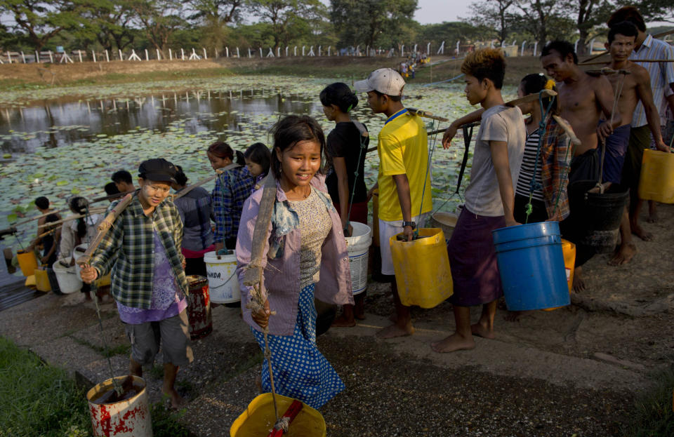 In this April 2, 2014 photo, residents of Dala, carry repurposed plastic containers filled with drinking water fetched from a natural water pond in the suburbs of Yangon, Myanmar. During the annual dry season in April and May, residents pay 10 kyat, or 10 U.S. cents for each bucket of water and walk up to five kilometers (three miles) carrying the buckets for their families in this improvised neighborhood. (AP Photo/Gemunu Amarasinghe)