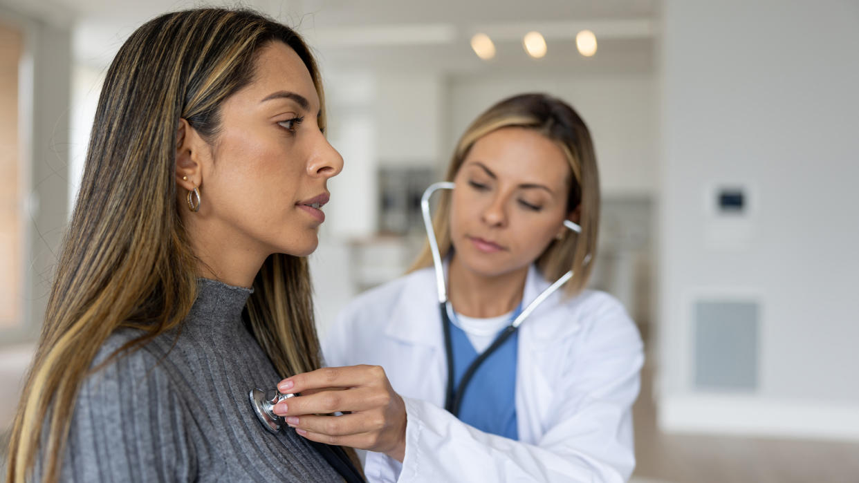  Doctor placing a stethoscope on a female patient's chest over the patient's sweater. 