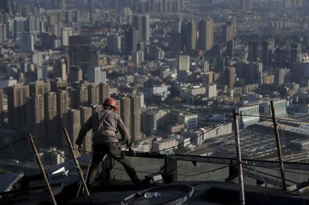 A labourer works atop a construction site of a commercial building as residential complexes are pictured in the background, in Kunming, Yunnan province, China, December 12, 2015. REUTERS/Wong Campion