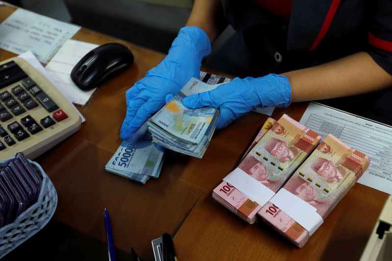 An employee wearing a face mask and synthetic gloves counts Indonesia's rupiah banknotes at a currency exchange office amid the spread of coronavirus disease (COVID-19) in Jakarta