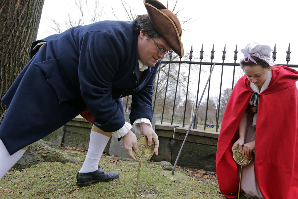 Actor-interpreters from the Boston Tea Party Ships and Museum, Tim Lawton and Jillian Couillard place commemorative markers, Tuesday, Nov. 27, 2018, at Central Burying Ground on Boston Common at the graves of participants in the Dec. 16, 1773 protest known as the Boston Tea Party. This year is the 245th anniversary of the protest during which colonists protesting taxation without representation threw British tea into Boston Harbor, considered a pivotal event that led to the American Revolution. (AP Photo/Elise Amendola)