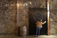 Stephanie Skoglund touches up paint on a giant chalk board where guests can leave messages for the bride and groom at The Vault, the wedding and event center she owns in Tenino, Wash., on July 1, 2020. The board still bears the names — Kyzer and Sandra — of the last couple to be married at the venue in March before the coronavirus outbreak forced them to close their doors. (AP Photo/Ted S. Warren)