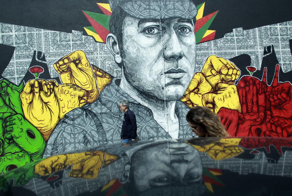 In this picture shot April 24 2014, people walk past a mural showing army captain Salgueiro Maia in Lisbon. Maia was one of the captains that led the soldiers taking part in the April 25 1974 revolution that restored democracy in Portugal. The mural was painted by 33-year old street artist Miguel Januario who said he held dear the changes brought by an event he didn't live through, "but since then we've allowed new forms of dictatorship, in this case financial, to take over." (AP Photo/Francisco Seco)
