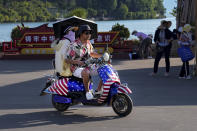 A Chinese couple ride on an electric bike with decals of the American flag, passing by visitors tour at Erhai lake in Dali, in southwestern China's Yunnan province on Saturday, July 16, 2022. China's government on Wednesday, July 27, rejected as a "political lie" a report by The Wall Street Journal that Beijing tried to recruit informants in the Federal Reserve system to obtain U.S. economic data. (AP Photo/Andy Wong)