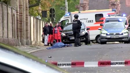 Police stand in a secured area with a covered body after a fatal shooting in Halle