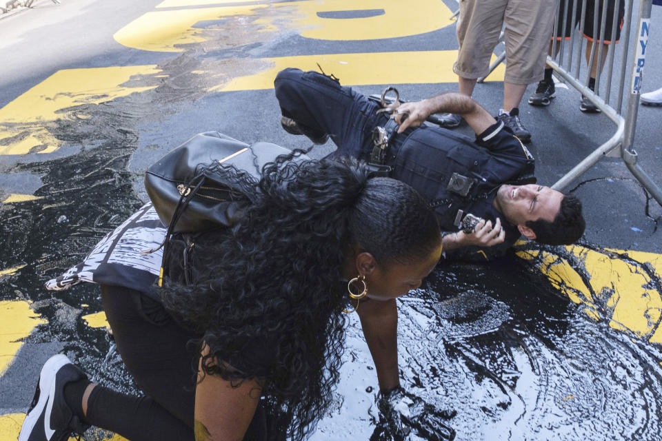 An NYPD officer falls during an attempt to detain a protester pouring black paint on the Black Lives Matter mural outside of Trump Tower on Fifth Avenue in the Manhattan borough of New York on Saturday, July 18, 2020. (AP Photo/Yuki Iwamura)