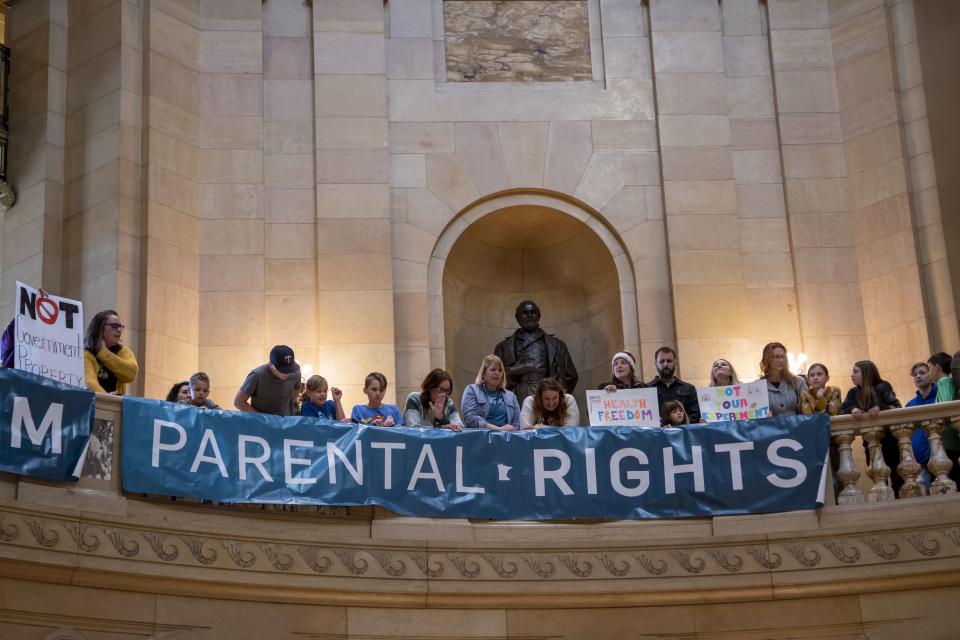 Protesters line a balcony with signs that read: We support health freedom and Parental rights.