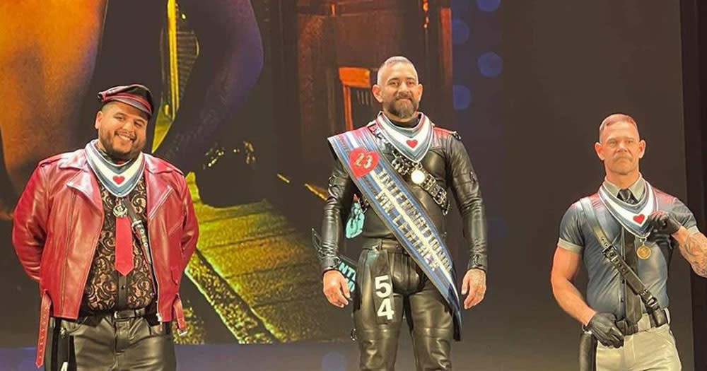 The image shows the three winners of the International Mr Leather contest 2023. On the left is a black man wearing a red leather jacket. In the middle is a latin X man wearing a black leather outfit with a sash and on the right is a man wearing a leather waistcoat.