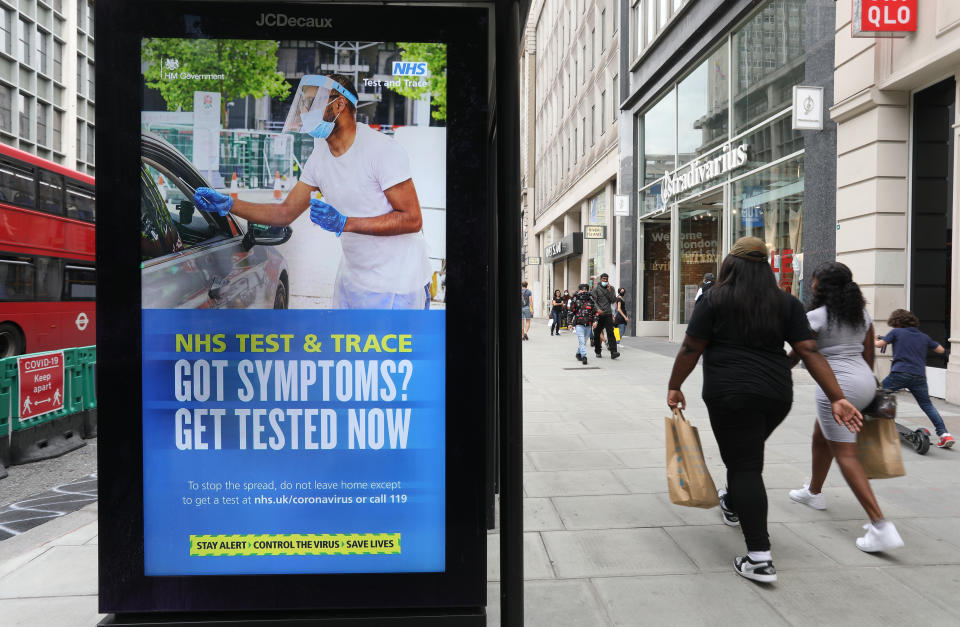 Shoppers walk past a screen on a bus stop displaying a NHS notice on test and trace on Oxford Street, London, as non-essential shops in England open their doors to customers for the first time since coronavirus lockdown restrictions were imposed in March. Picture date: Monday June 15, 2020.