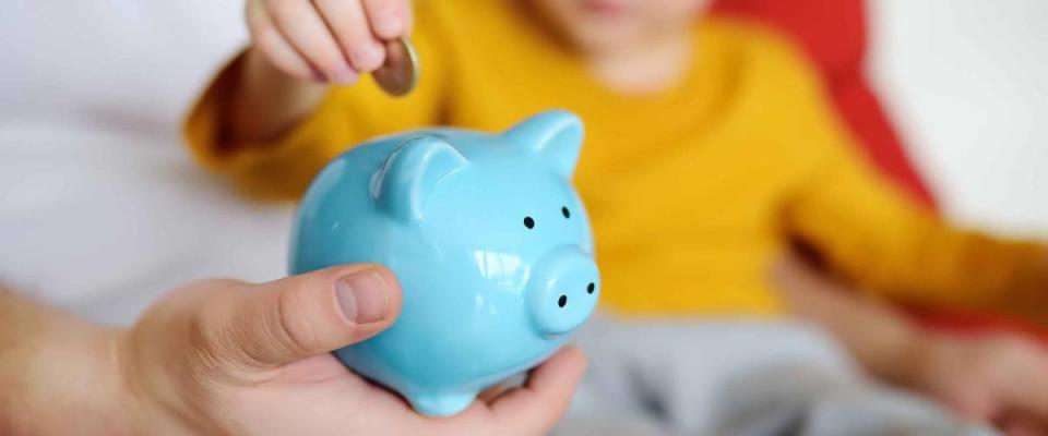 Father and child putting coin into piggy bank.