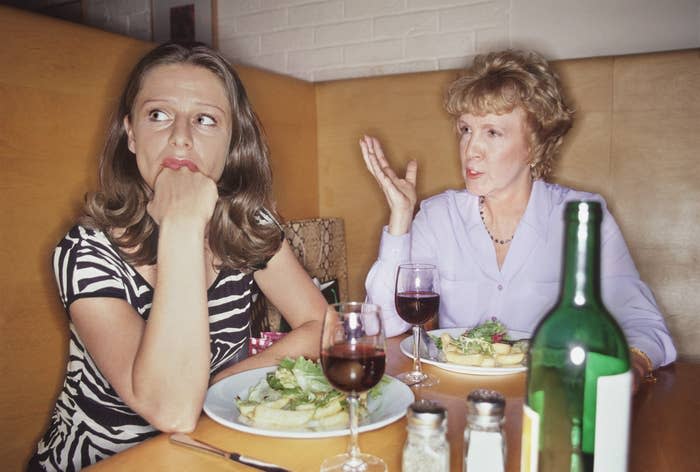 Two women engaged in a conversation at a restaurant table with plates of food and a wine bottle