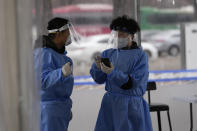 Health workers wearing protective gears prepare for visitors at a temporary screening clinic for the coronavirus in Seoul, South Korea, Tuesday, Jan. 25, 2022. South Korea recorded more than 8,000 new coronavirus infections for the first time Tuesday as health authorities reshape the country's pandemic response to address a surge driven by the highly contagious omicron variant. (AP Photo/Lee Jin-man)