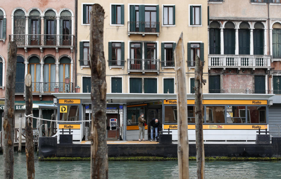 In this picture taken on Wednesday, May 13, 2020, people wearing a sanitary mask wait for a ferry in Venice, Italy. Venetians are rethinking their city in the quiet brought by the coronavirus pandemic. For years, the unbridled success of Venice's tourism industry threatened to ruin the things that made it an attractive destination to begin with. Now the pandemic has ground to a halt Italy’s most-visited city, stopped the flow of 3 billion euros in annual tourism-related revenue and devastated the city's economy. (AP Photo/Antonio Calanni)