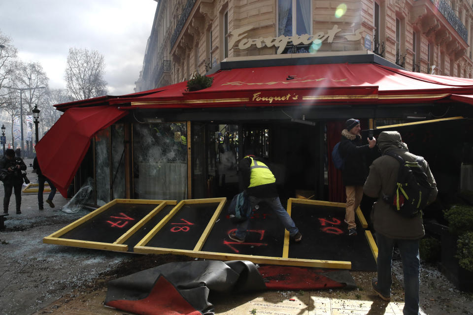 Protesters enter the famed restaurant Fouquet's, damaged after clashes, on the Champs Elysees avenue, during a yellow vests demonstration Saturday, March 16, 2019 in Paris. Paris police say more than 100 people have been arrested amid rioting in the French capital by yellow vest protesters and clashes with police. They set life-threatening fires, smashed up luxury stores and clashed with police firing tear gas and water cannon (AP Photo/Christophe Ena)