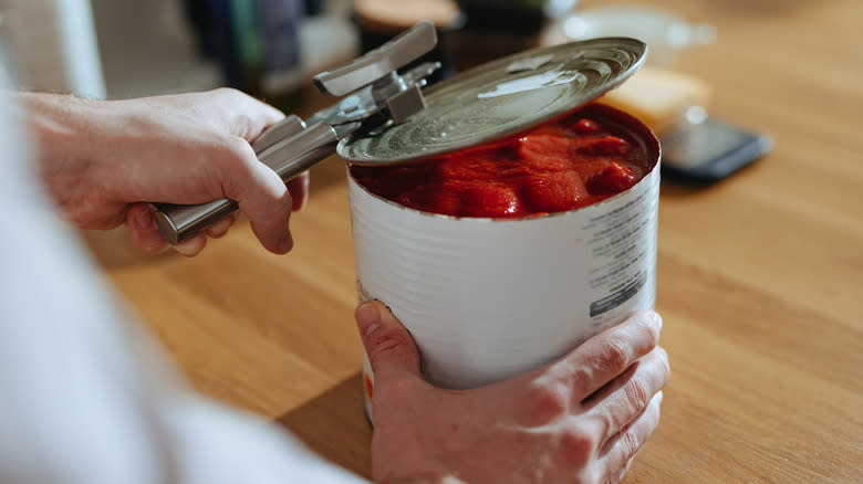 Person opening canned tomatoes