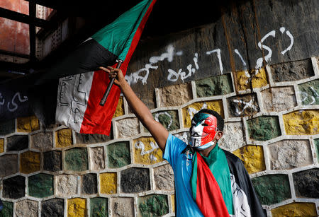 A protester holding a Sudanese flag and wearing a Guy Fawkes mask takes part in a demonstration in front of the Defence Ministry in Khartoum, Sudan April 17, 2019. REUTERS/Umit Bektas