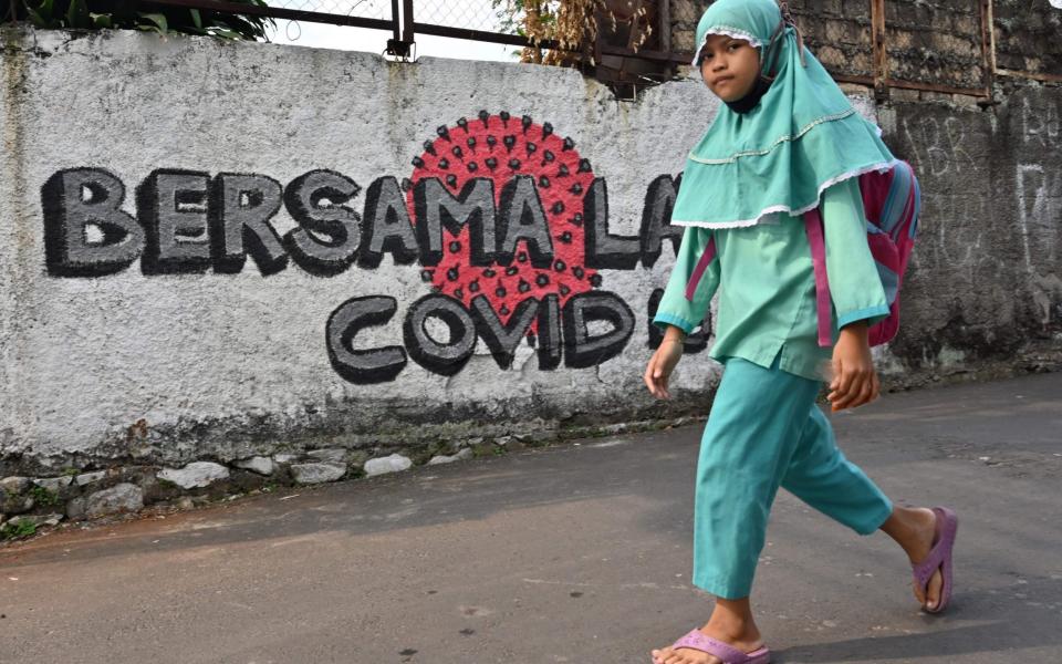An Indonesian girl walks past a sign that says "together against Covid" - Adek Berry/AFP