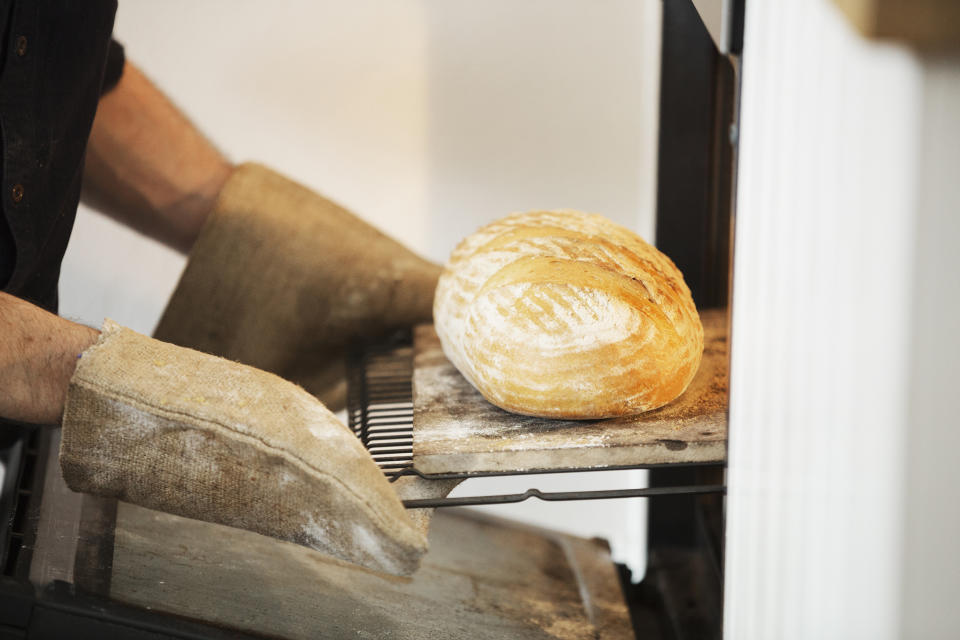 Close up of a baker taking a freshly baked loaf bread out of an oven. (Getty Images stock)