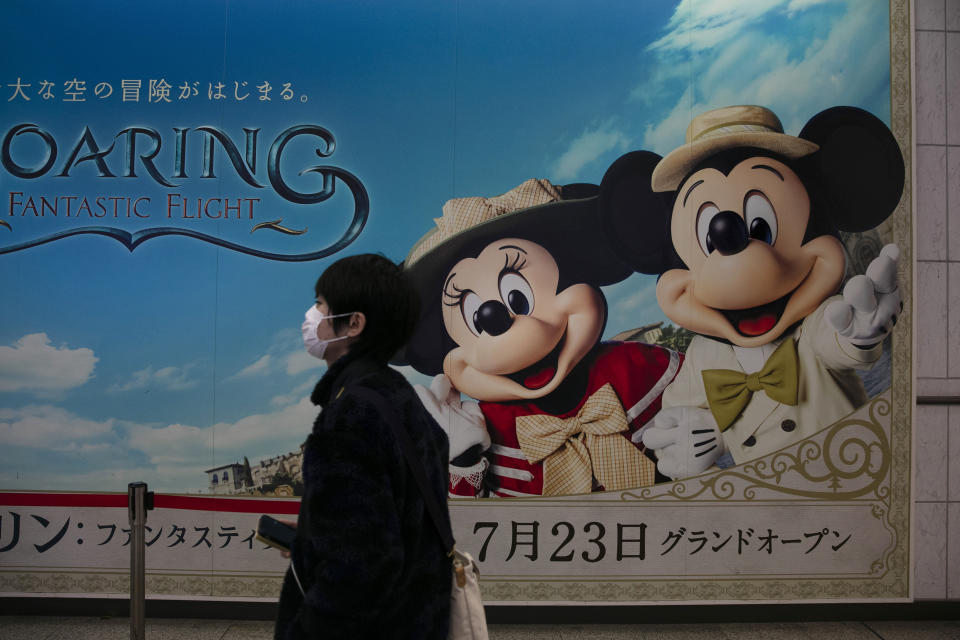 Un hombre con una mascarilla sobre la boca pasa por delante de un anuncio del parque de Disney en Tokio, en una estación de tren en Urayasu, cerca de Tokio, el 28 de febrero de 2020. (AP Foto/Jae C. Hong)