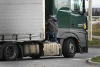 A migrant jumps on a truck in Calais, northern France, Thursday, Oct. 14, 2021, to cross the tunnel heading to Britain. In a dangerous and potentially deadly practice, he is trying to get through the heavily policed tunnel linking the two countries by hiding on a truck. (AP Photo/Christophe Ena)