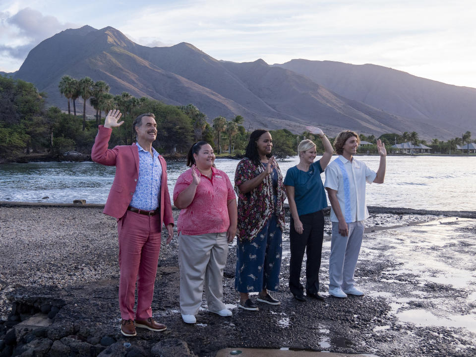 Five people standing on a beach waving, with mountains in the background