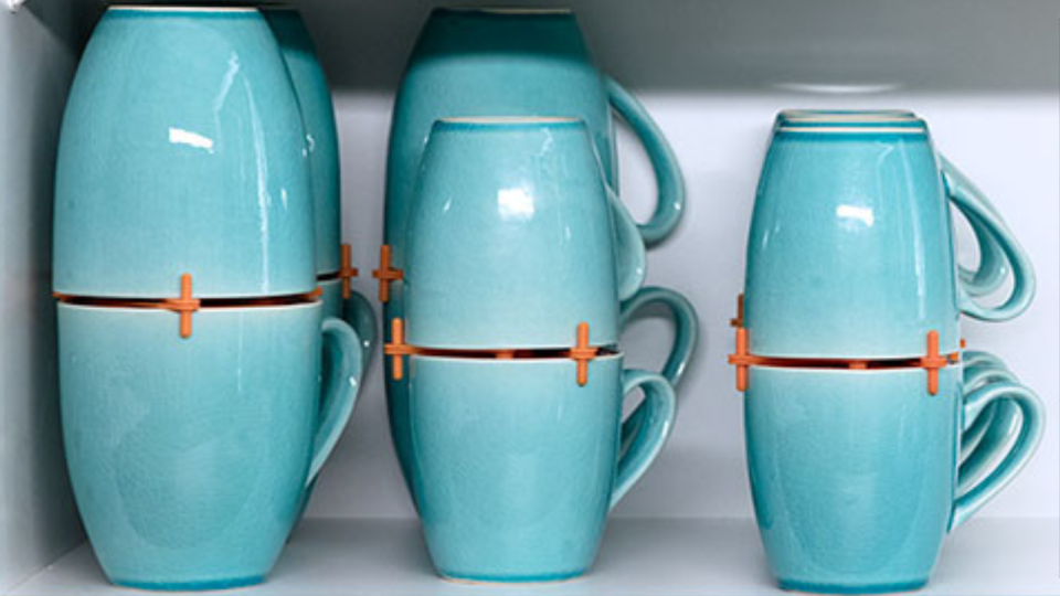 blue mugs neatly stored atop one another in a cabinet via orange mug organizers 